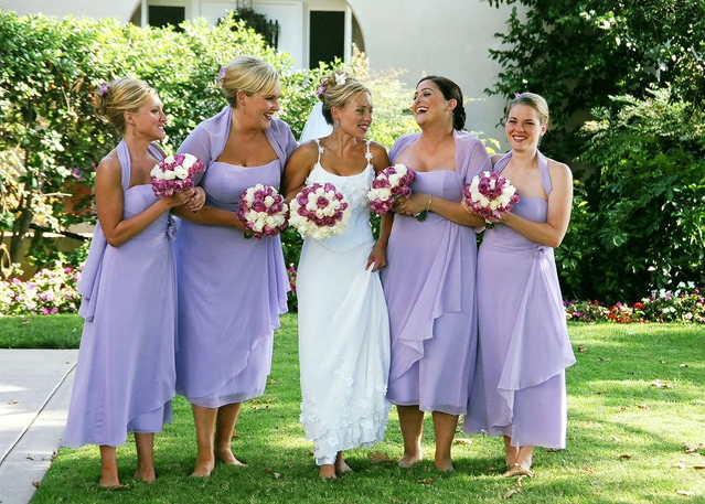 Bride and four bridesmaids laughing while standing in grass.