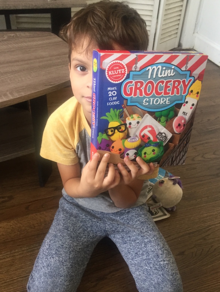 Aaron holding the Mini Grocery Store kit to his face. hiding his left eye with it.