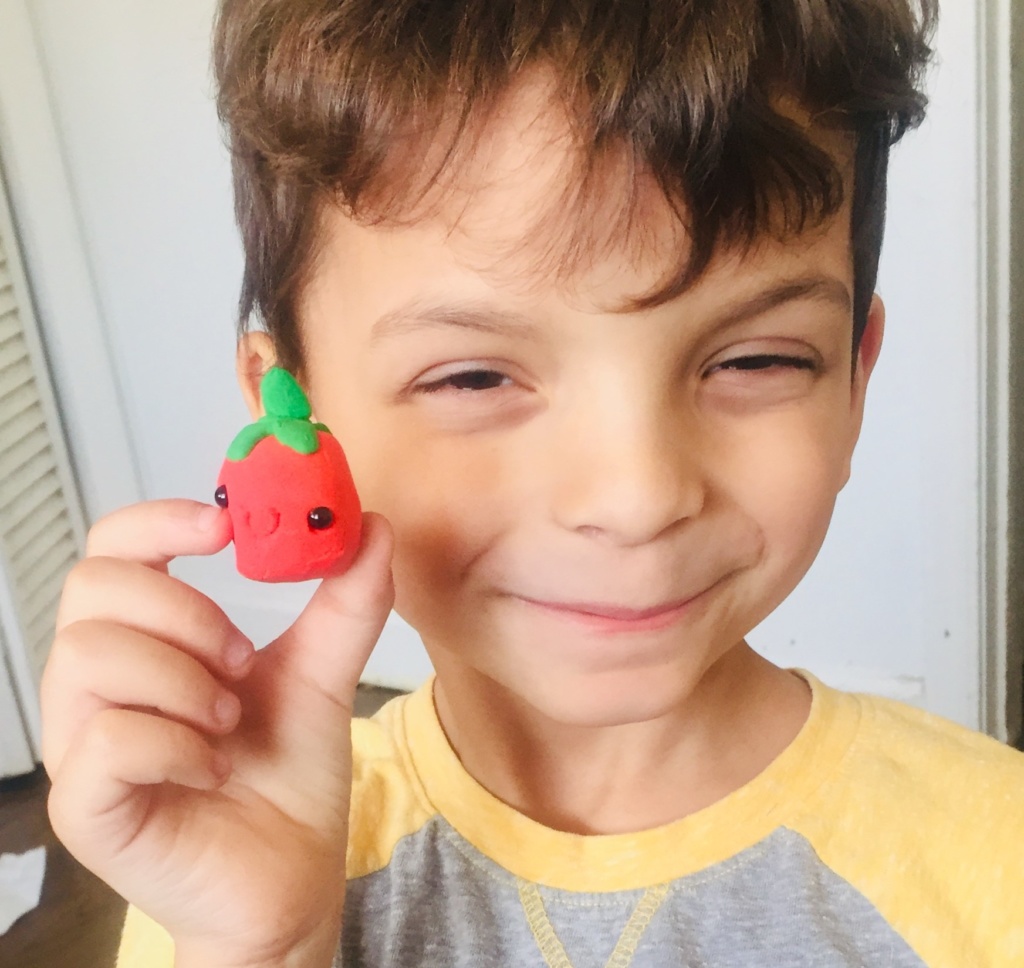 Aaron smiling and holding the smiley face clay tomato he made