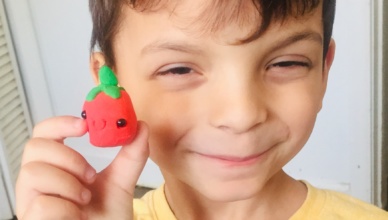 Aaron smiling and holding the smiley face clay tomato he made