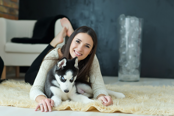 puppy owners - Caucasian woman with long straight black hair is smiling while laying on her stomach with her white and black puppy laying in front of her.